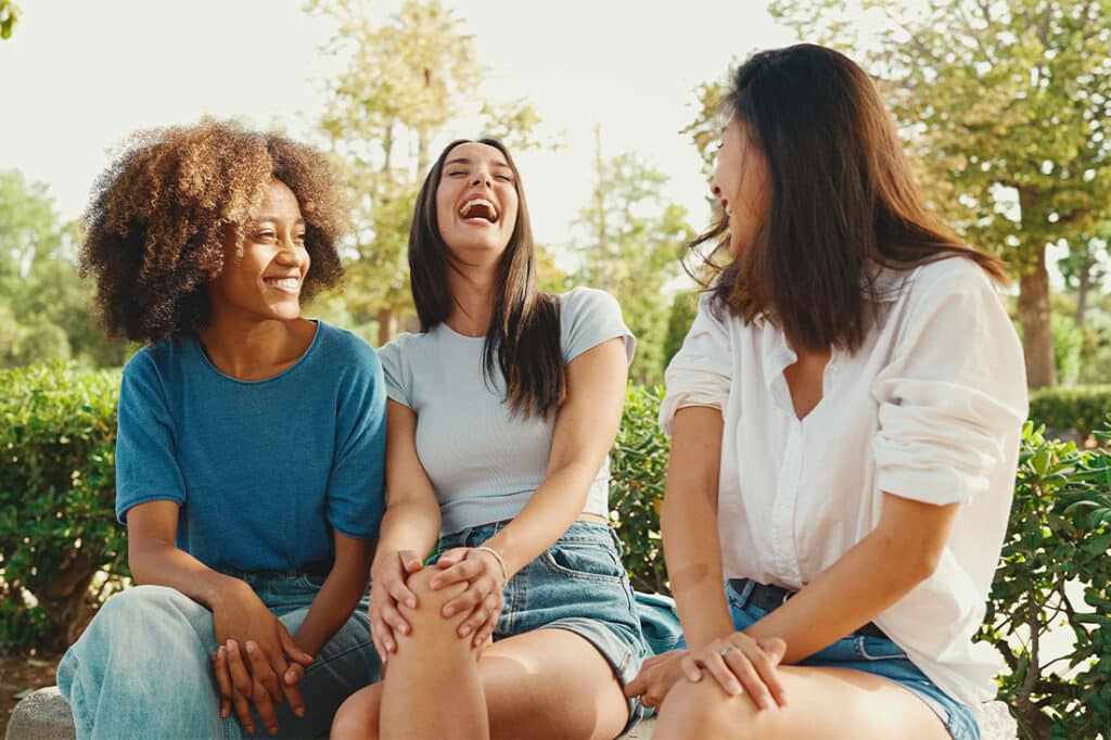 Group of young women talking while sitting on park bench on summer day outdoors