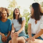 Group of young women talking while sitting on park bench on summer day outdoors