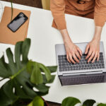 Overview of hands of young businesswoman or student typing on laptop keyboard by desk