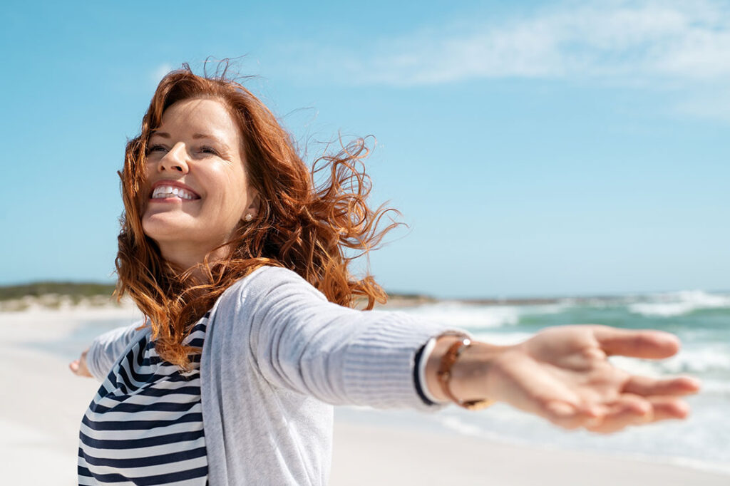Happy mature woman with arms outstretched feeling the breeze at beach