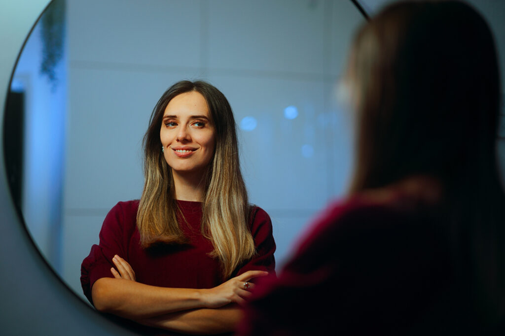 A confident woman smiles at her reflection in a mirror