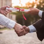 Cropped image of graduate in academic dress taking his diplomas and shaking hand, earning a degree