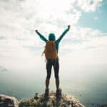 Successful hiker outstretched arms at seaside mountain top cliff edge