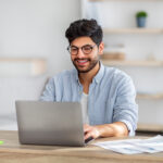 A male freelancer smiles and works on his laptop