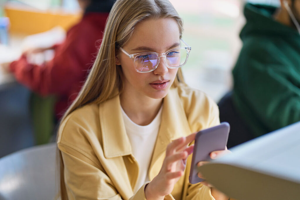 gen z woman using mobile phone looking at smartphone sitting at desk
