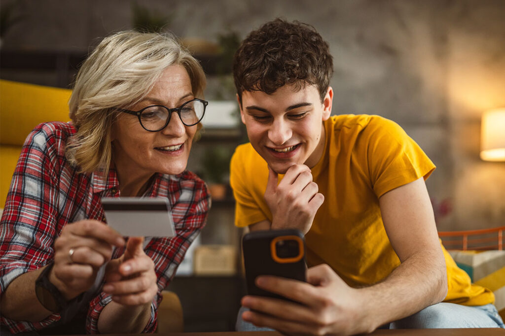 blonde woman and her teenager son shopping online use mobile phone and credit card