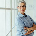 An empowered woman who has learned to embrace uncertainty stands in her office with her arms crossed