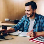 Man taking notes and working on laptop