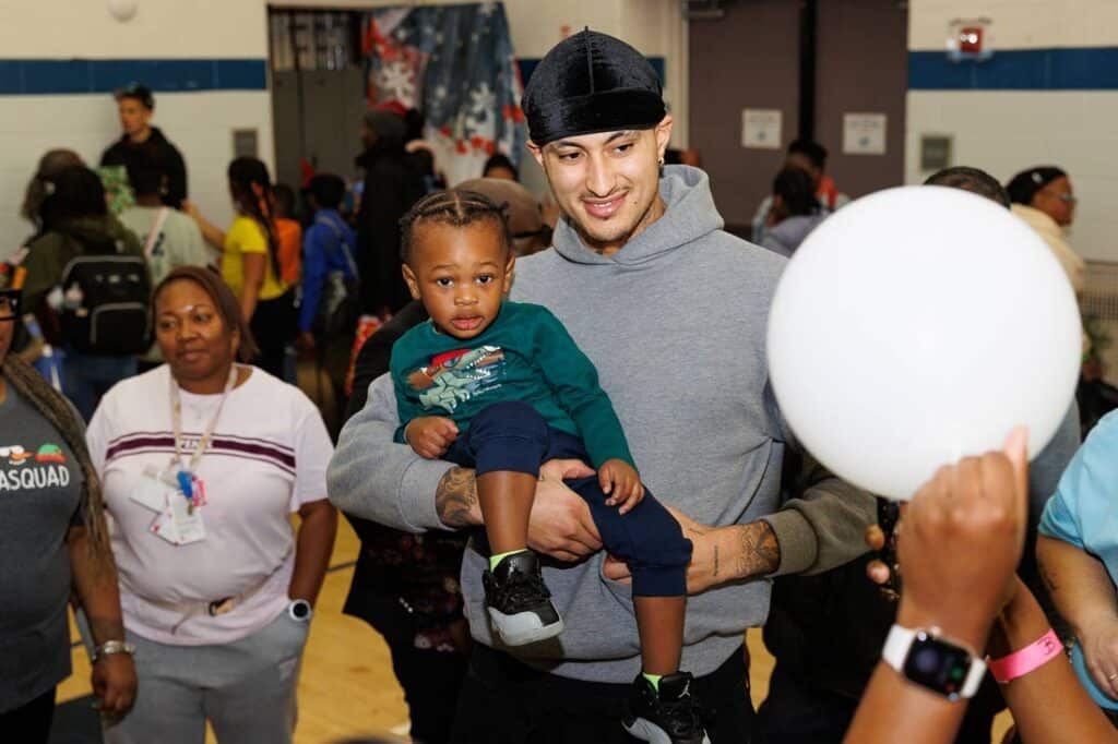 Kyle Kuzma holding a toddler and smiling