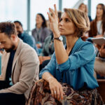 Female entrepreneur raising her hand to answer a question during business conference in convention center