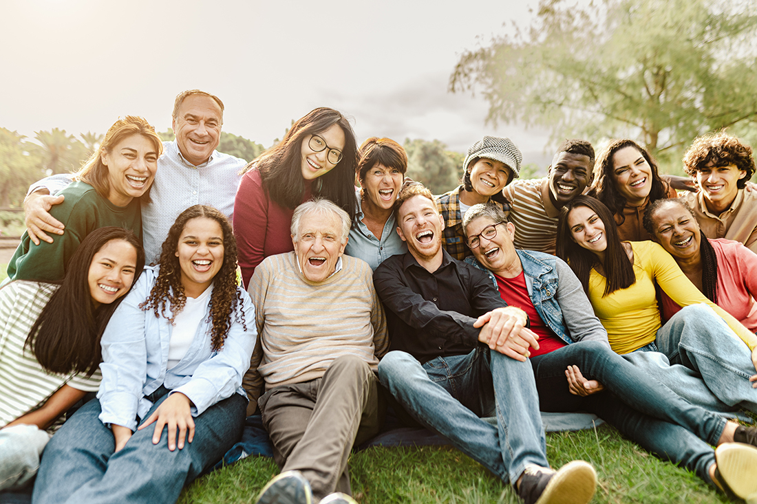 Happy intergenerational friends having fun sitting on grass in a public park