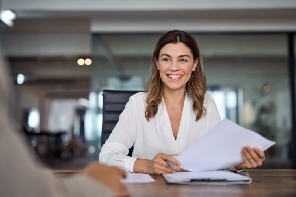 A smiling woman holds a resume and a pen.
