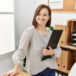 A young woman with down syndrome holds a clipboard in her office.