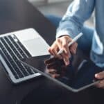 Hands holding up an iPad next to a laptop.