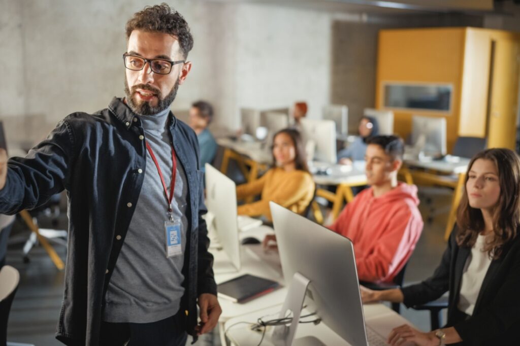 A teacher gives a lecture to rows of students at computers.