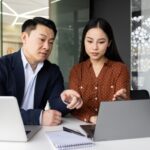 A man and woman point at a computer screen.