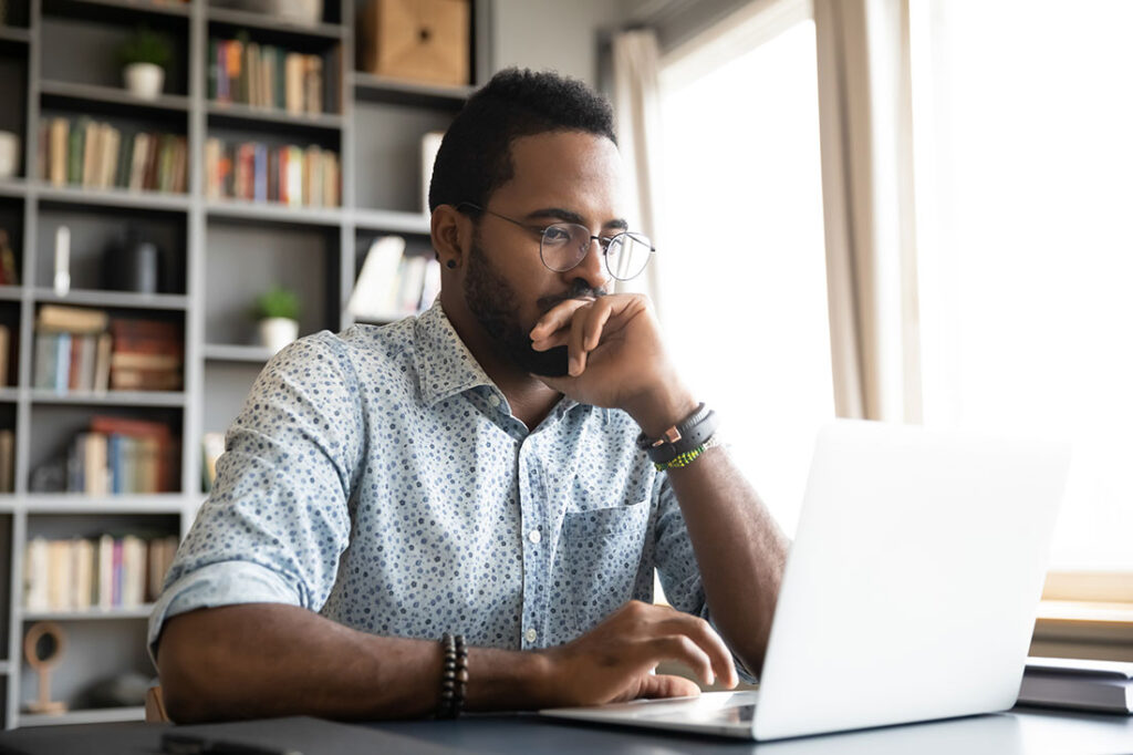 Focused young businessman sits at desk looking at laptop