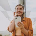 a woman wearing headphones and holding a smartphone while listening to an audiobook
