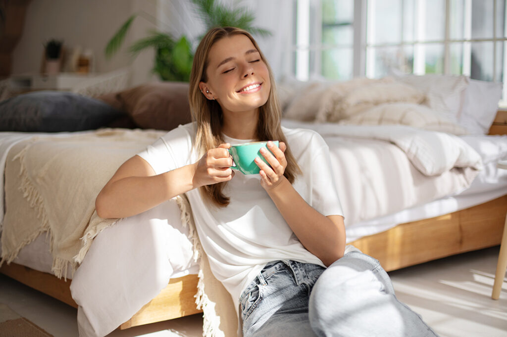 A smiling woman holds a cup of tea and enjoys being present in time
