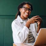 Smiling productive woman drinking coffee on her laptop