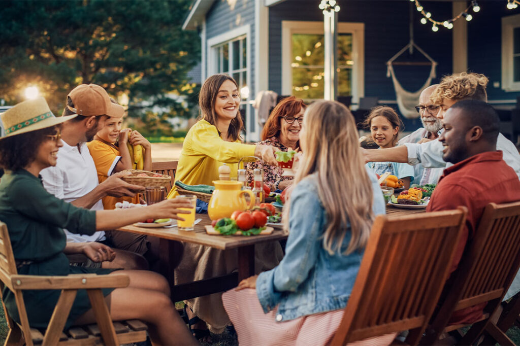 Group of friends or family gathering for a meal outdoors surrounding a table