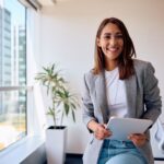 a businesswoman in an office smiling at the camera while holding a tablet device