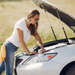 A woman in sunglasses leans over an opened car hood.